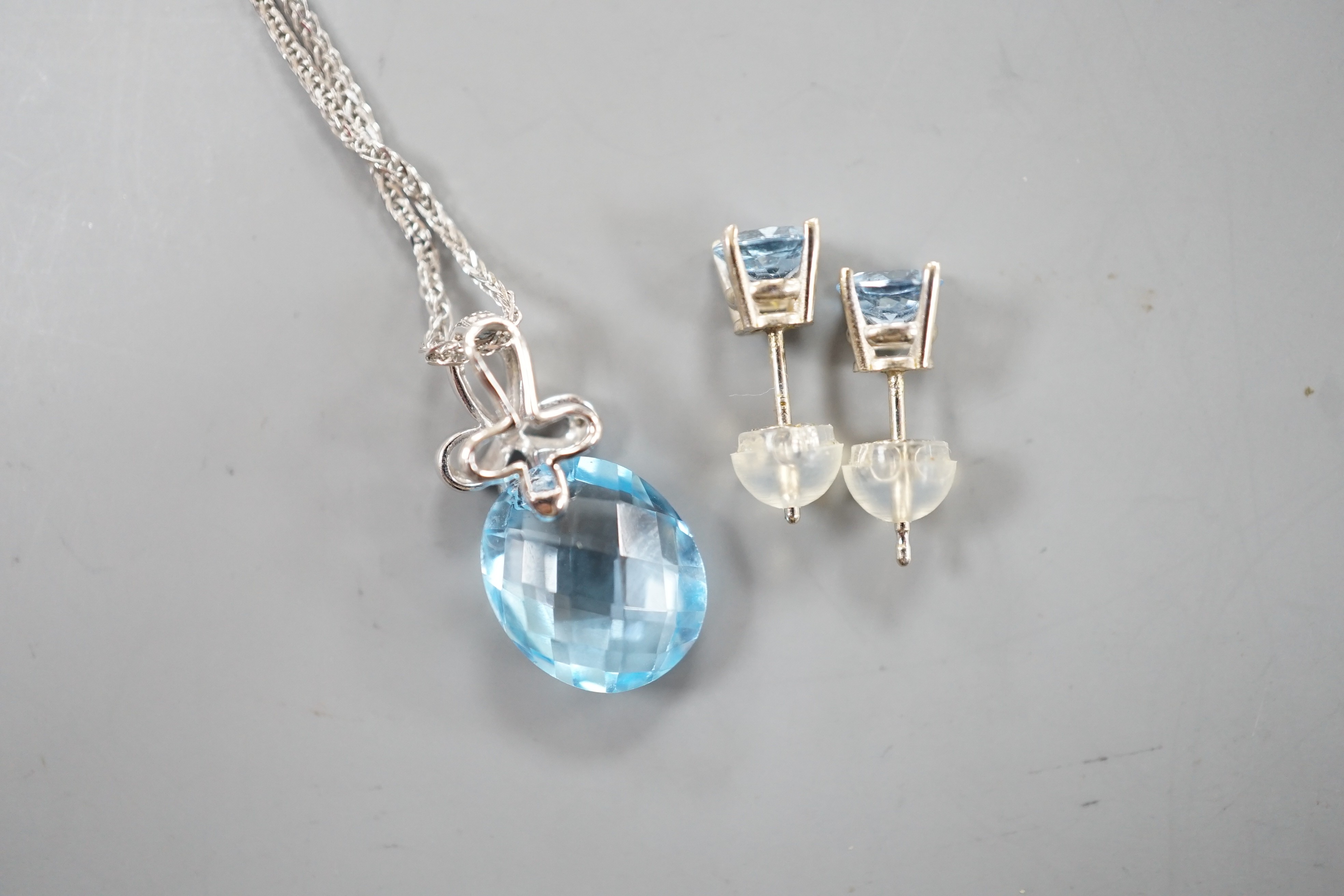 A modern 14k white metal, facetted pear cut blue topaz and diamond chip set pendant, 19mm, on a 750 white metal chain, 44cm and a pair 14k and blue topaz ear studs, gross weight 5.1 grams.